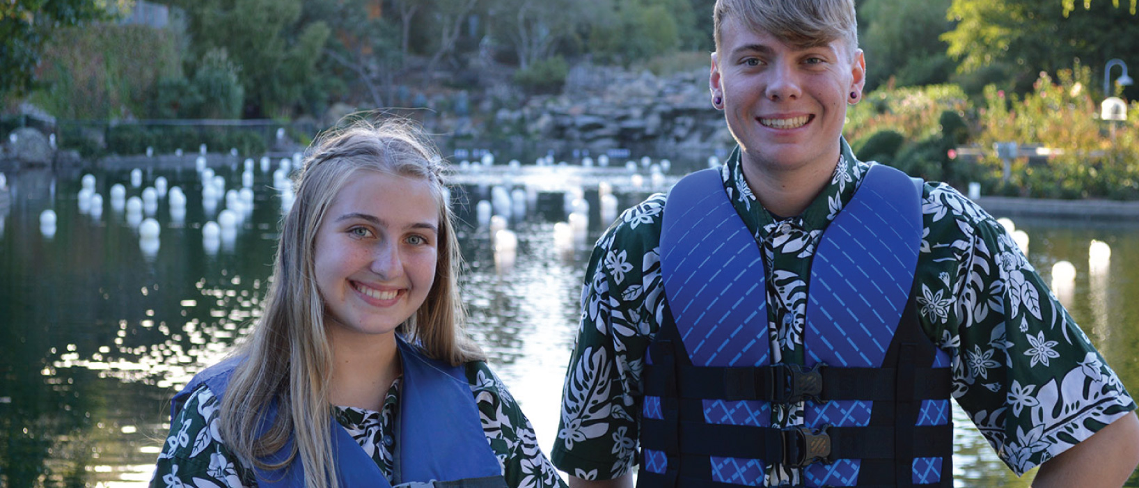 Two employees wearing blue life jackets smiling in front of Coyote Lake