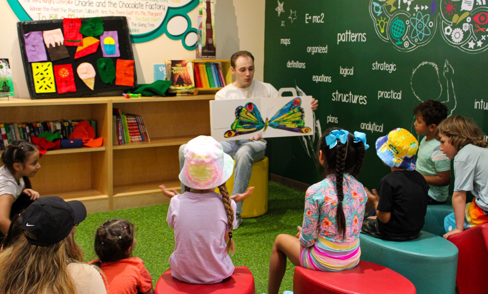 Man holding a book and reading a book about a butterfly to a room of young students